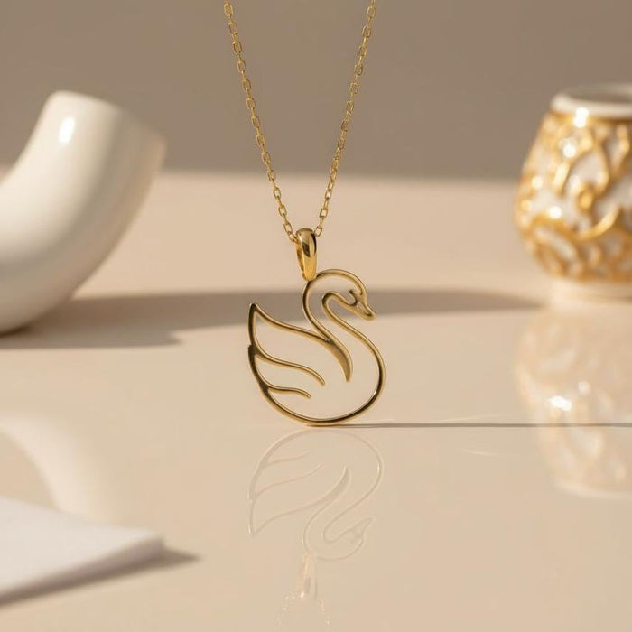 Gold Plated Silver openwork swan pendant displayed on a reflective cream surface