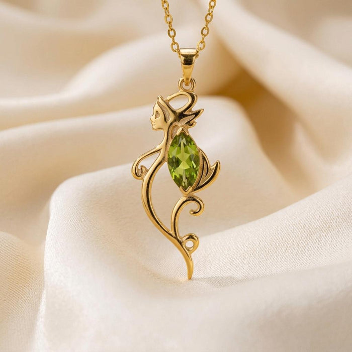 Close-up of a Gold Plated Silver pointed-ear elf pendant with a green marquise-cut center stone on light fabric