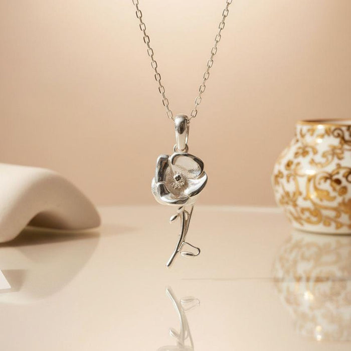 Silver Poppy Flower Necklace hanging against a warm neutral background