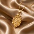 Gold Plated Silver Queen Aura Pendant with crowned side-profile portrait and ornate oval frame on champagne satin