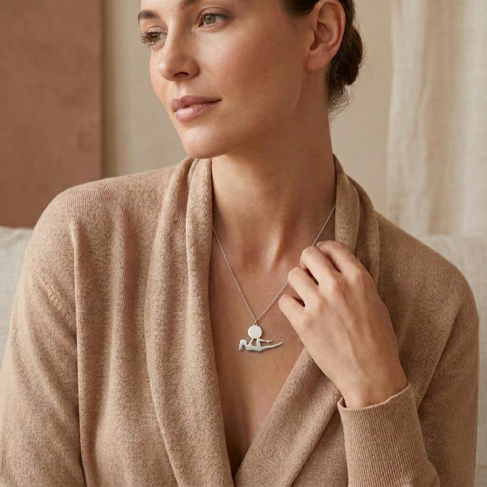 Reclining yoga figure pendant necklace worn with a tan wrap cardigan