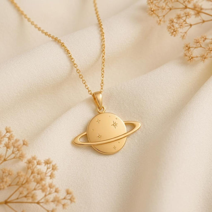 Gold-toned Saturn pendant necklace displayed on ivory satin with dried floral accents