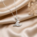 Silver Sea Wave Necklace with a layered curling wave pendant on champagne satin beside small white flowers