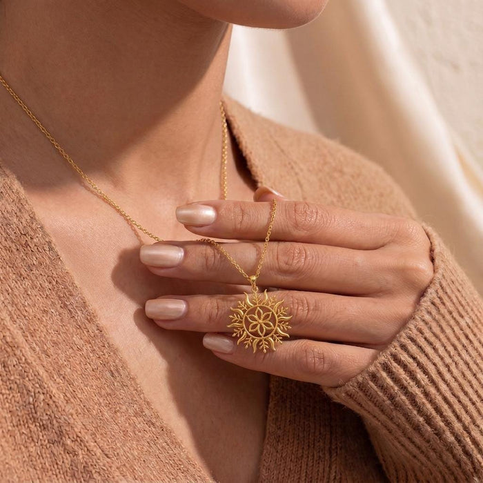 Gold Plated Silver Solstice Bloom pendant necklace held at the neckline over a neutral knit top