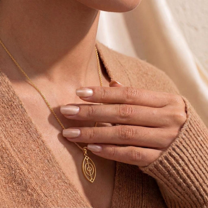 Close view of a model holding a Gold Plated Silver Spirit Gate Pendant necklace at the neckline
