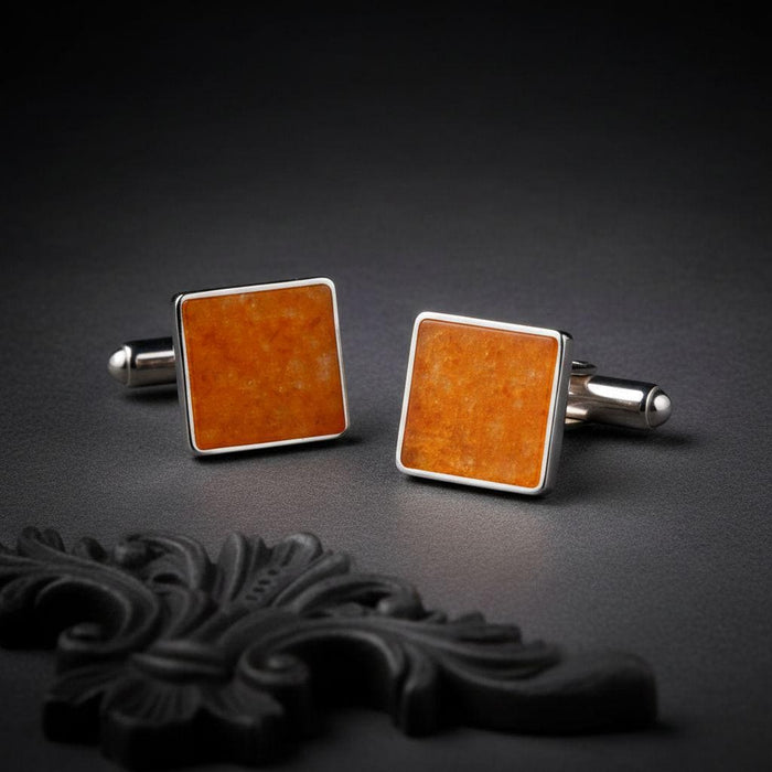 Pair of square amber cufflinks with orange-toned panels and polished borders on a dark textured surface
