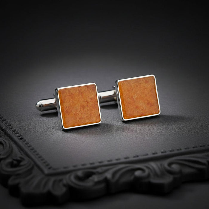 Pair of square amber cufflinks with polished borders on a dark textured surface with decorative edging