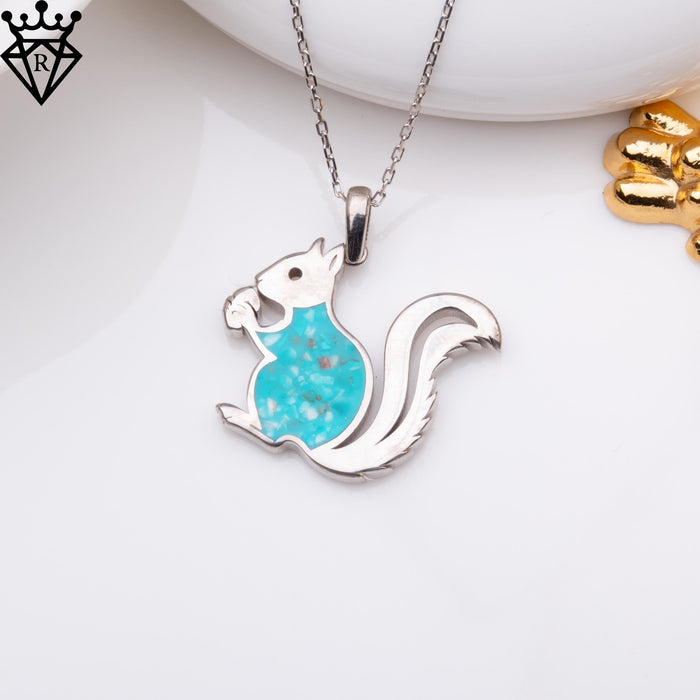 Turquoise squirrel necklace displayed beside a white dish and gold accents