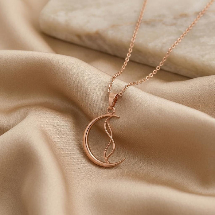 Rose Gold Plated Whisper Crescent Pendant necklace on champagne satin beside a pale stone