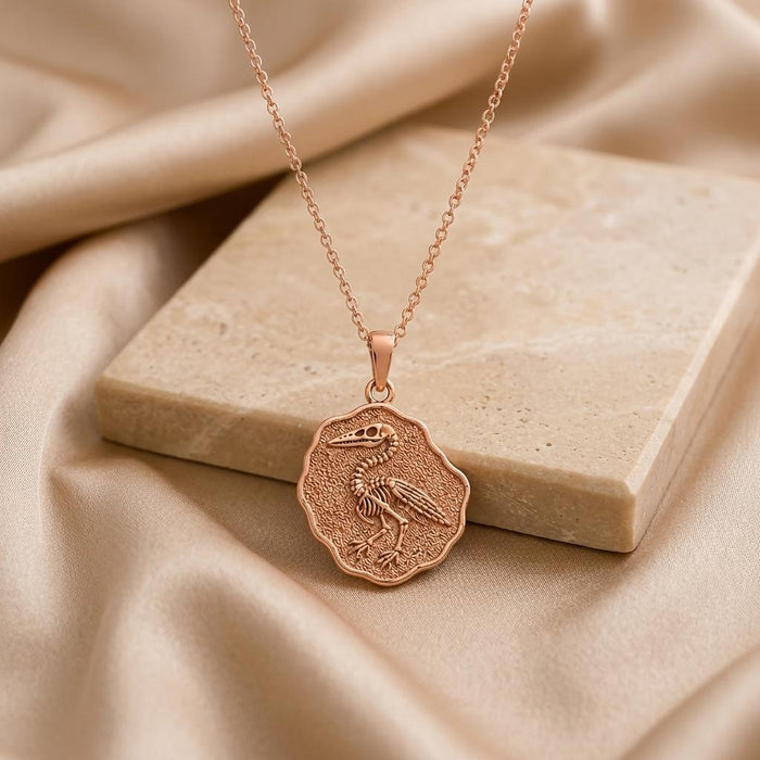 Rose Gold Plated Ichthyornis fossil medallion necklace with raised bird skeleton on a stone block