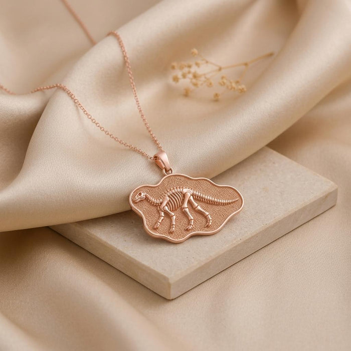Rose Gold Plated Iguanodon Fossil Pendant Necklace on cream satin with a textured irregular fossil-style plaque
