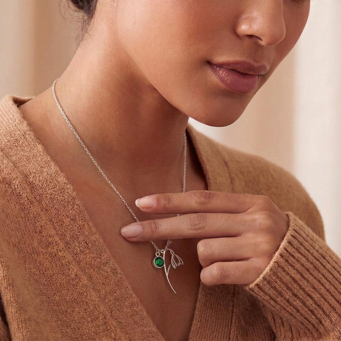 Close-up of a silver snowdrop-inspired flower necklace with curved stem and green round stone