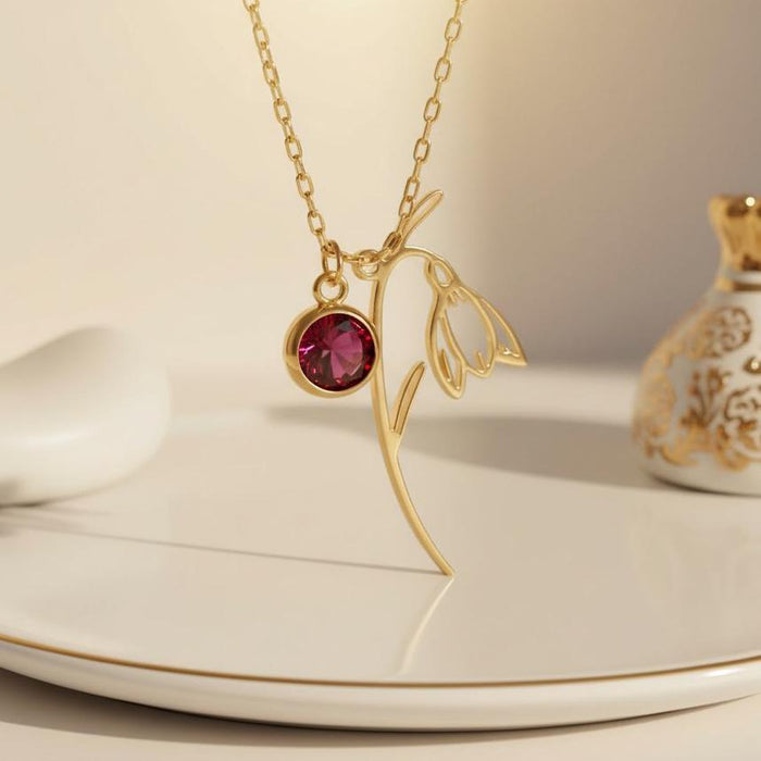 Gold Plated Silver January Birth Flower Necklace with a snowdrop-inspired bloom and red round stone on a display surface