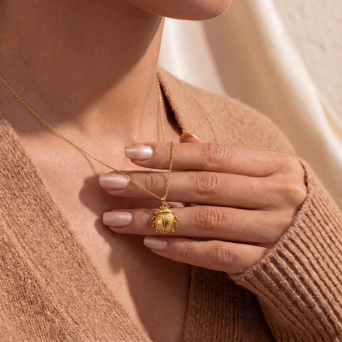 Ladybug Necklace in Gold Plated Silver worn at the neckline while a hand holds the rounded pendant