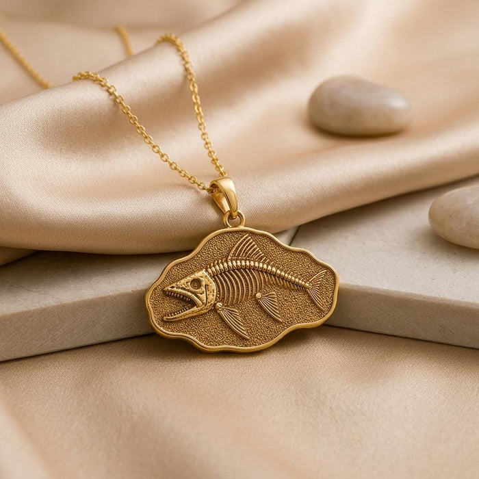 Gold-finish Leedsichthys Fossil Pendant Necklace with a fish skeleton relief on champagne satin beside smooth stones