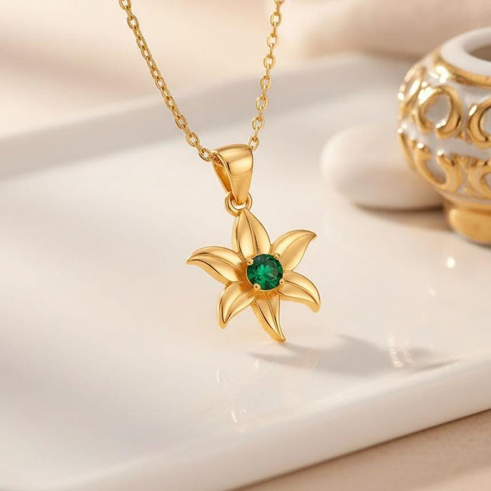 Gold Plated Silver Lily Birth Flower Necklace with six sculpted petals and a green center stone on a white display