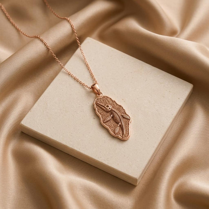 Rose Gold Plated Liopleurodon Fossil Pendant Necklace displayed on a square stone block with draped fabric
