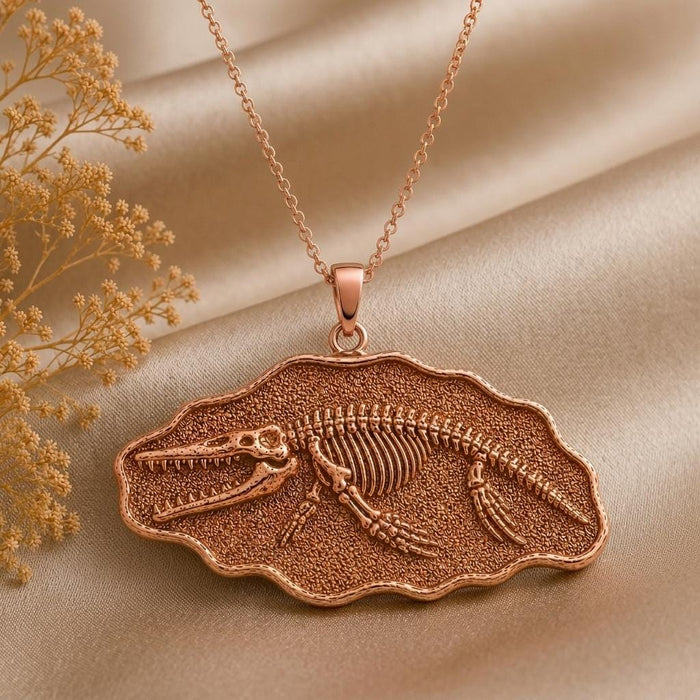 Rose Gold Plated Livyatan Fossil Pendant Necklace with a raised skeletal motif on beige satin beside dried flowers