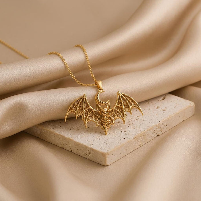 Gold-toned Lunar Bat Relic pendant necklace arranged on champagne satin and a pale stone slab