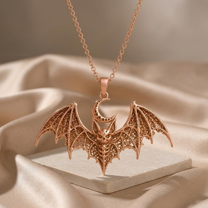 Rose-toned Lunar Bat Relic pendant necklace suspended above a pale stone block and neutral satin