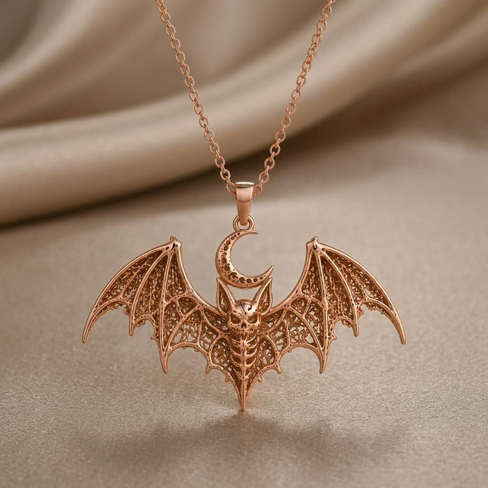 Close product view of a rose-toned Lunar Bat Relic pendant necklace on neutral fabric