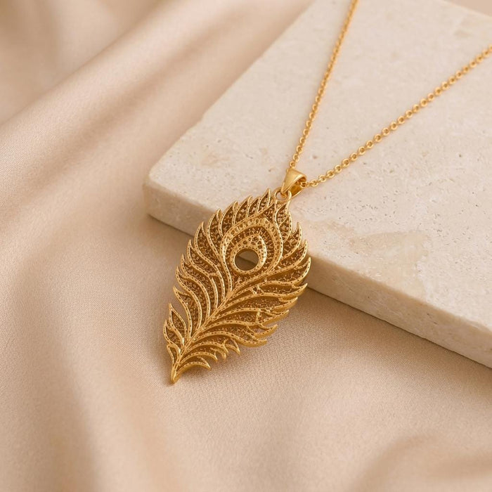 Gold Plated Silver Lunar Peacock Relic pendant necklace displayed beside a pale stone slab on satin