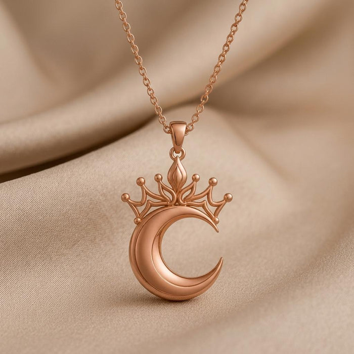 Rose-tone crowned crescent pendant necklace displayed on folded beige fabric