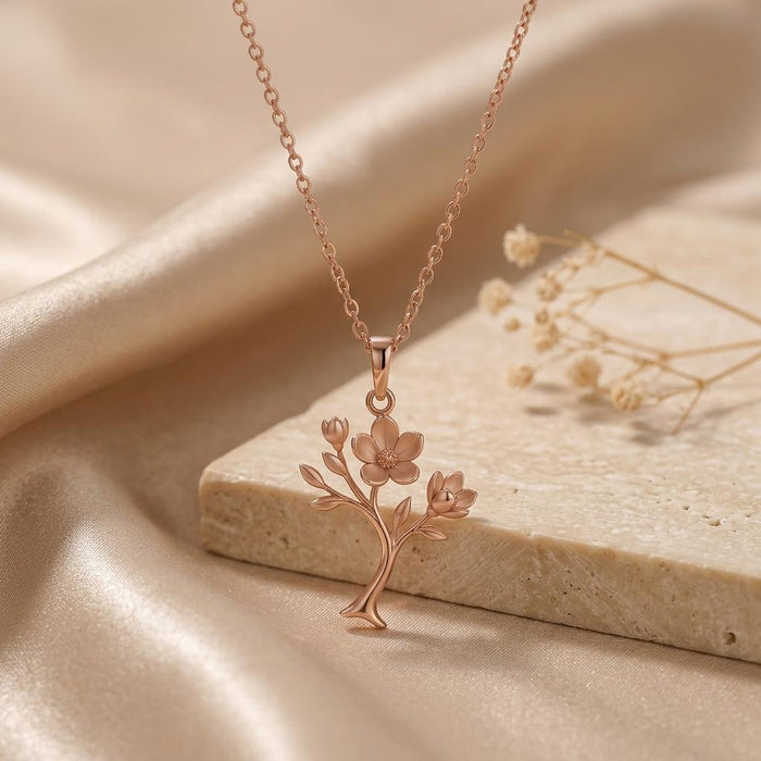 Rose Gold Plated Magnolia Soft Bloom Pendant beside a stone slab and dried flowers