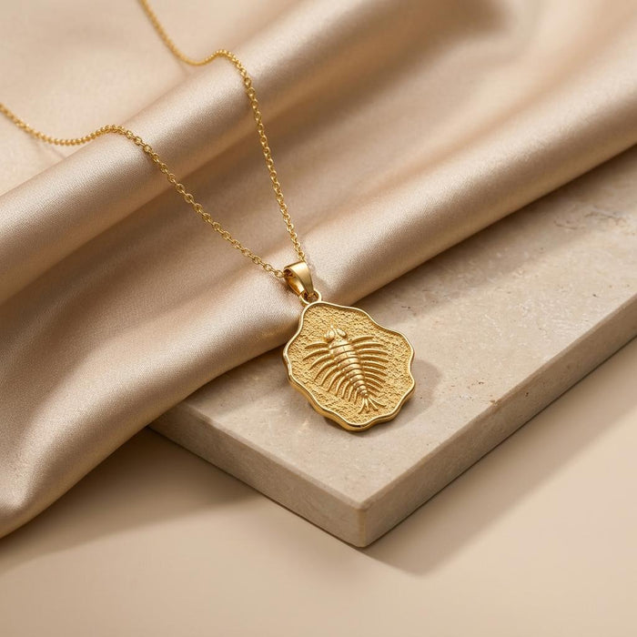Gold Plated Silver Marella fossil pendant arranged on champagne satin beside a stone block