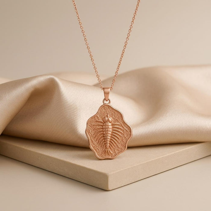 Rose Gold Plated Marella fossil pendant displayed upright on a pale stone block and champagne satin