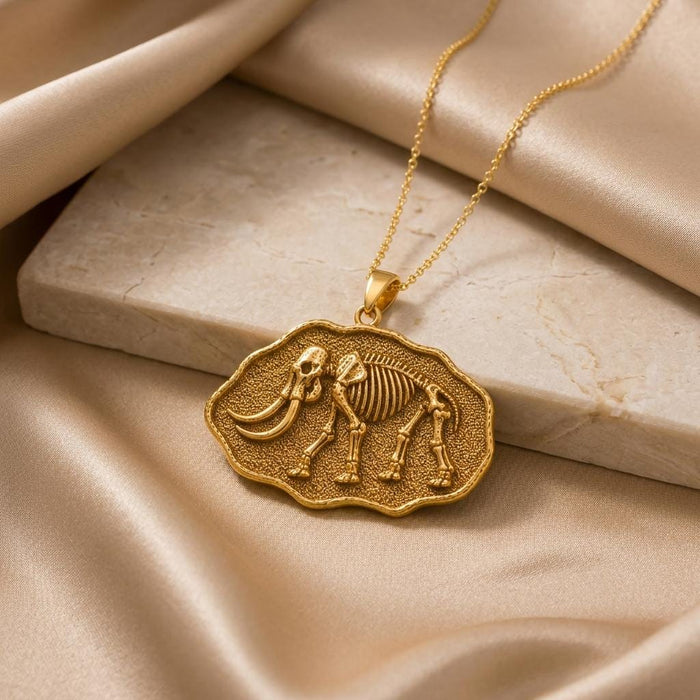 Gold Plated Silver mastodon skeleton fossil pendant necklace beside a pale stone block and champagne satin
