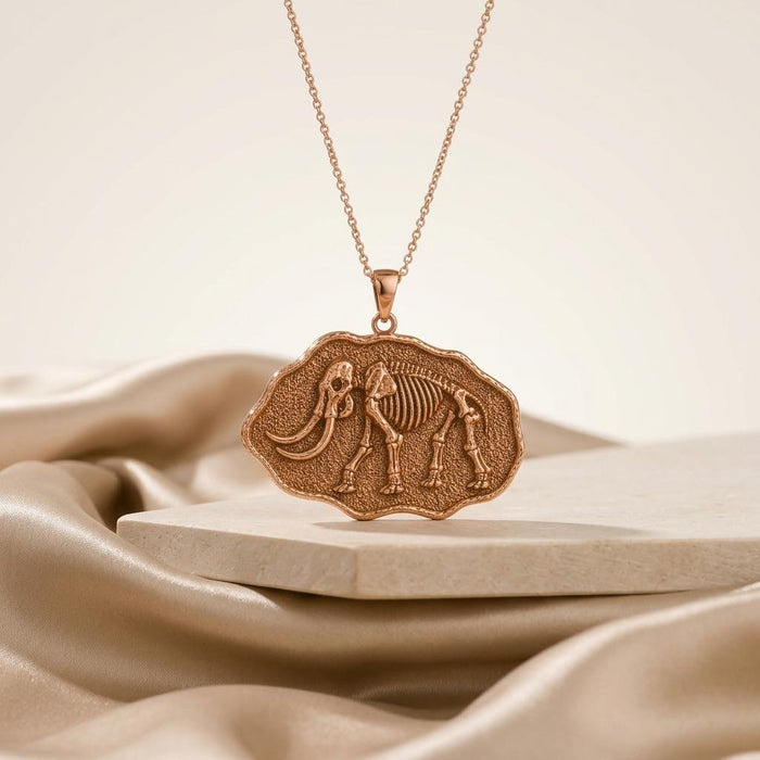 Rose Gold Plated mastodon skeleton fossil pendant necklace on a pale stone platform with champagne satin