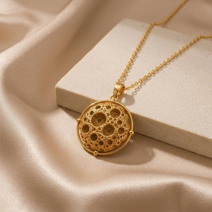 Gold Plated Silver Mathilde Asteroid Pendant Necklace with crater-textured sphere displayed beside a light stone block on champagne satin