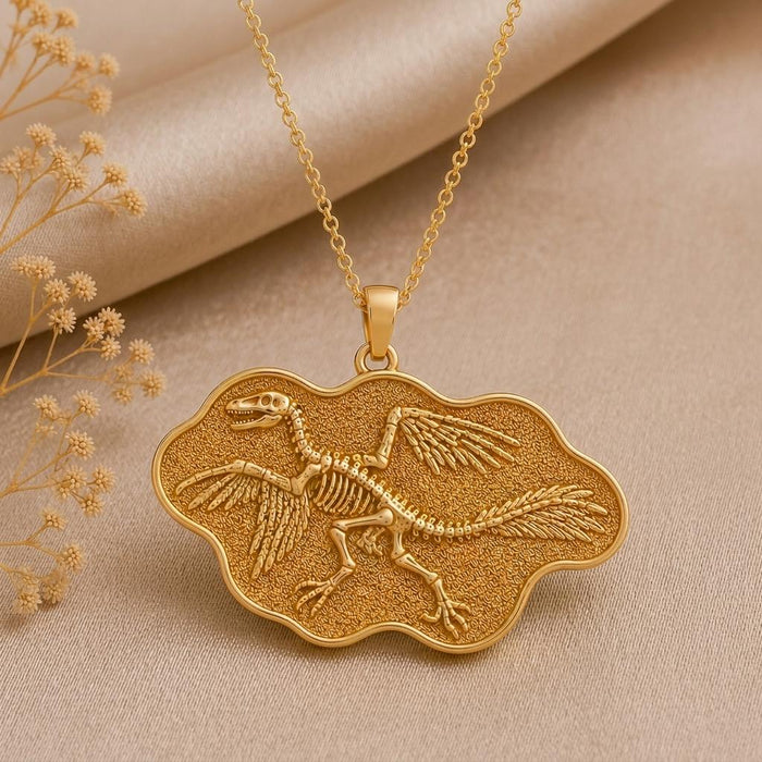 Close view of a Gold Plated Silver Microraptor skeleton relief in a textured scalloped pendant frame