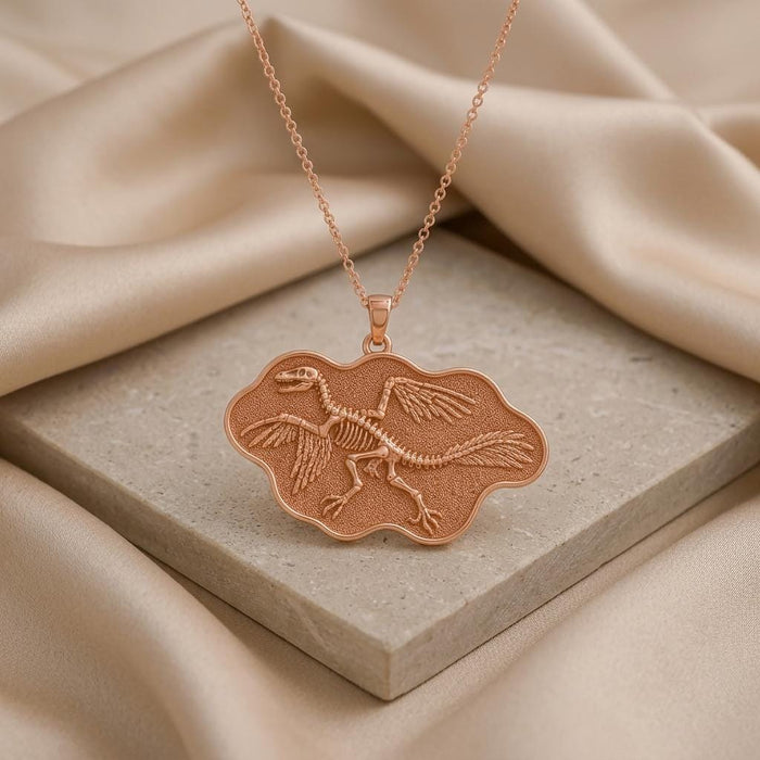 Rose Gold Plated Microraptor fossil pendant displayed on a square stone surface