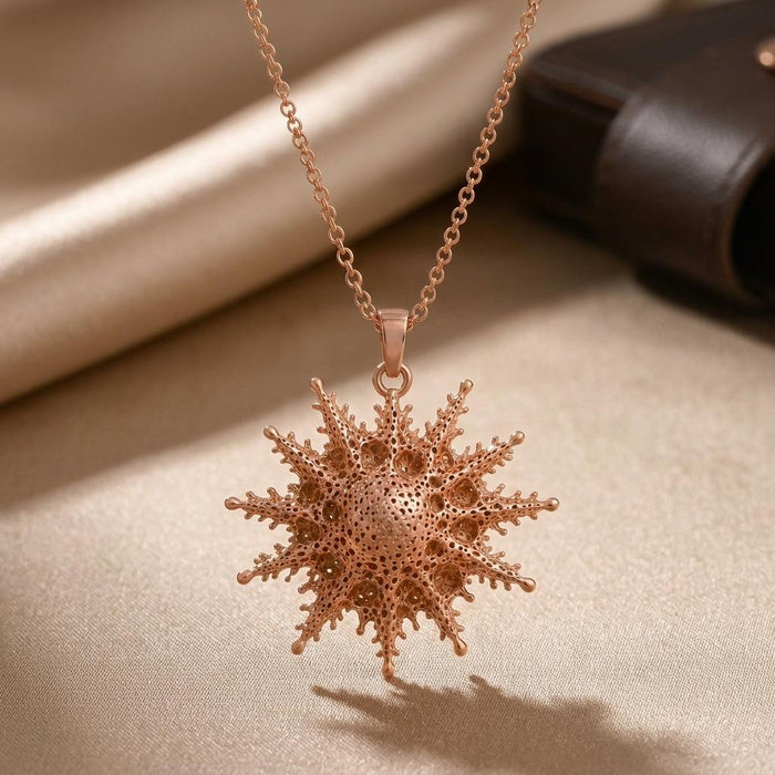 Rose-tone Mintaka star pendant necklace on satin beside a dark cylindrical prop