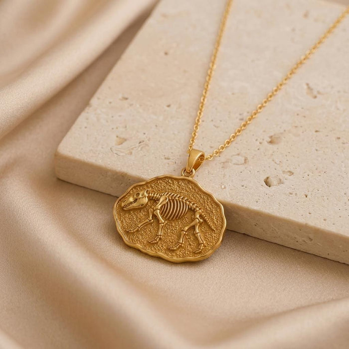 Gold-finish Moeritherium skeleton relief pendant beside a pale stone block