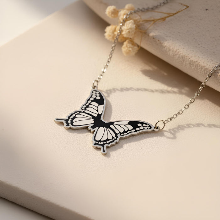 Flat-lay product image of the Monarch Butterfly Necklace on a cream surface with dried flowers