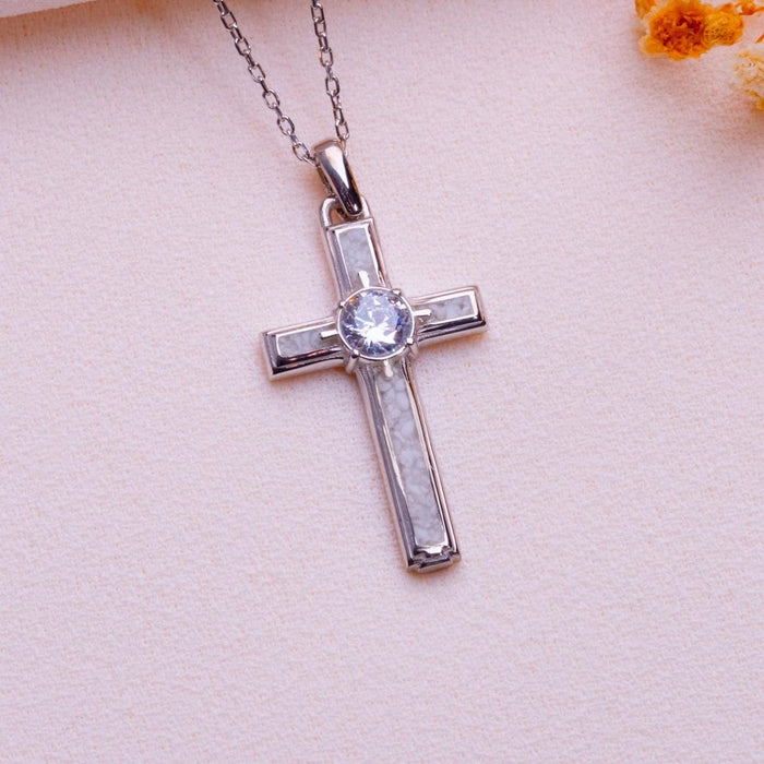Moonstone Cross Necklace with framed pale panels and a round center stone on pale textured fabric beside an orange flower