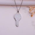 Moonstone key pendant necklace in a silver finish on pale blush fabric beside dried flowers