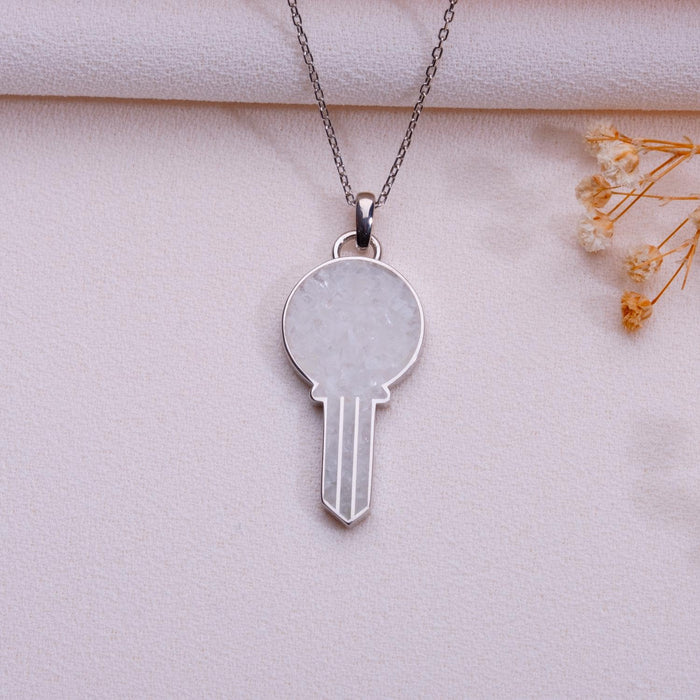 Moonstone key pendant necklace in a silver finish on pale blush fabric beside dried flowers