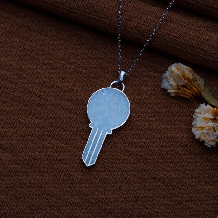 Moonstone key pendant necklace arranged on brown fabric beside dried flowers