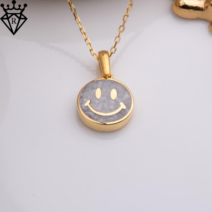 Moonstone smiley pendant on a white surface with chain visible and a small gold-toned decorative prop at the upper edge