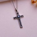 Onyx cross pendant necklace with framed rectangular arm sections and a dark round center stone on pale textured fabric