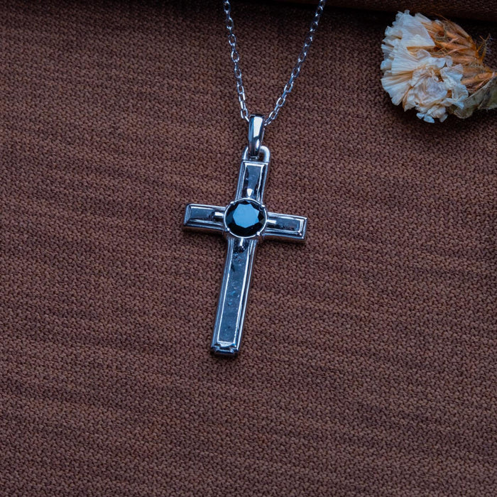 Onyx cross necklace with a dark round center stone on brown woven fabric beside dried flowers