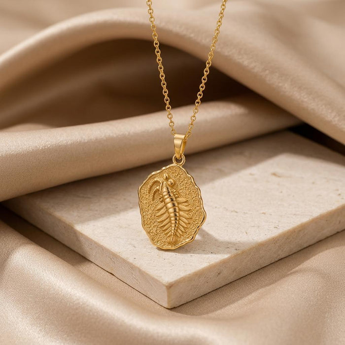Gold Plated Silver Opabinia fossil pendant necklace displayed on a pale stone block with draped satin
