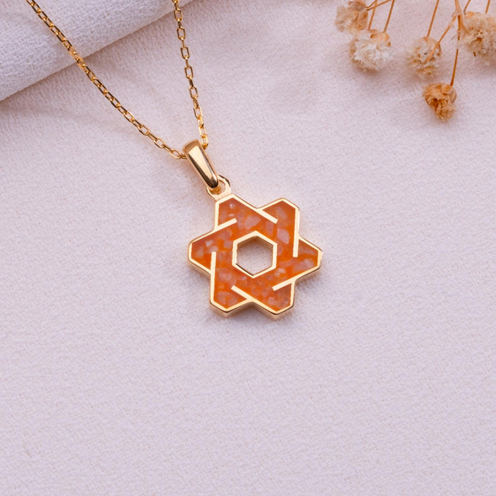 Orange agate six-point star pendant necklace on pale fabric beside dried flowers