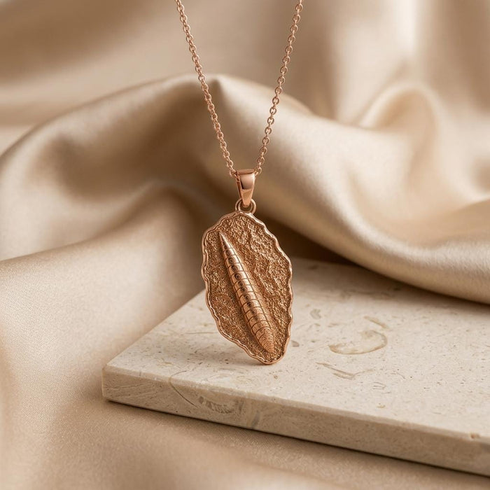 Rose Gold Plated Orthoceras Fossil Pendant Necklace displayed on a pale stone block with champagne satin