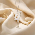 Close-up of the Figure Skater Necklace on cream satin, showing both hands holding a raised skate above the skater’s head