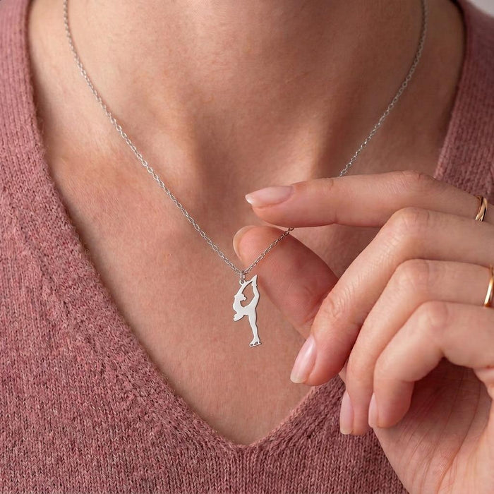 Figure Skater Necklace worn over a pink knit V-neck top, with a hand beside the overhead skate-hold pendant